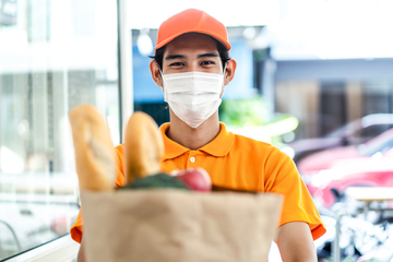 Asian deliver man wearing face mask in orange uniform holding bag of food.
