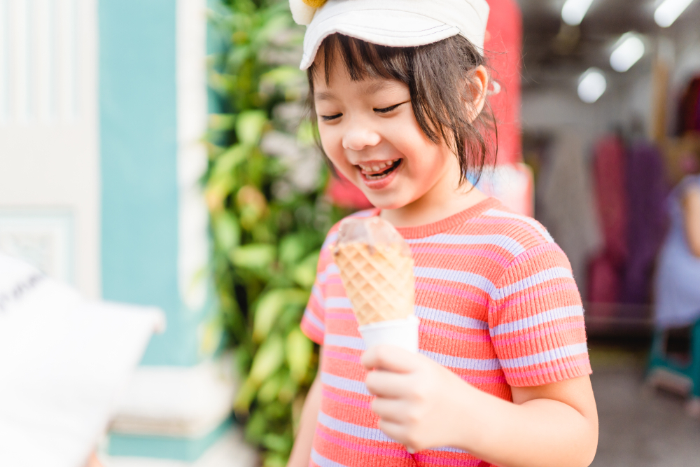 Happy Little asian girl walking and enjoy eating chocolate soft cream cone or ice cream cone at street in summer season